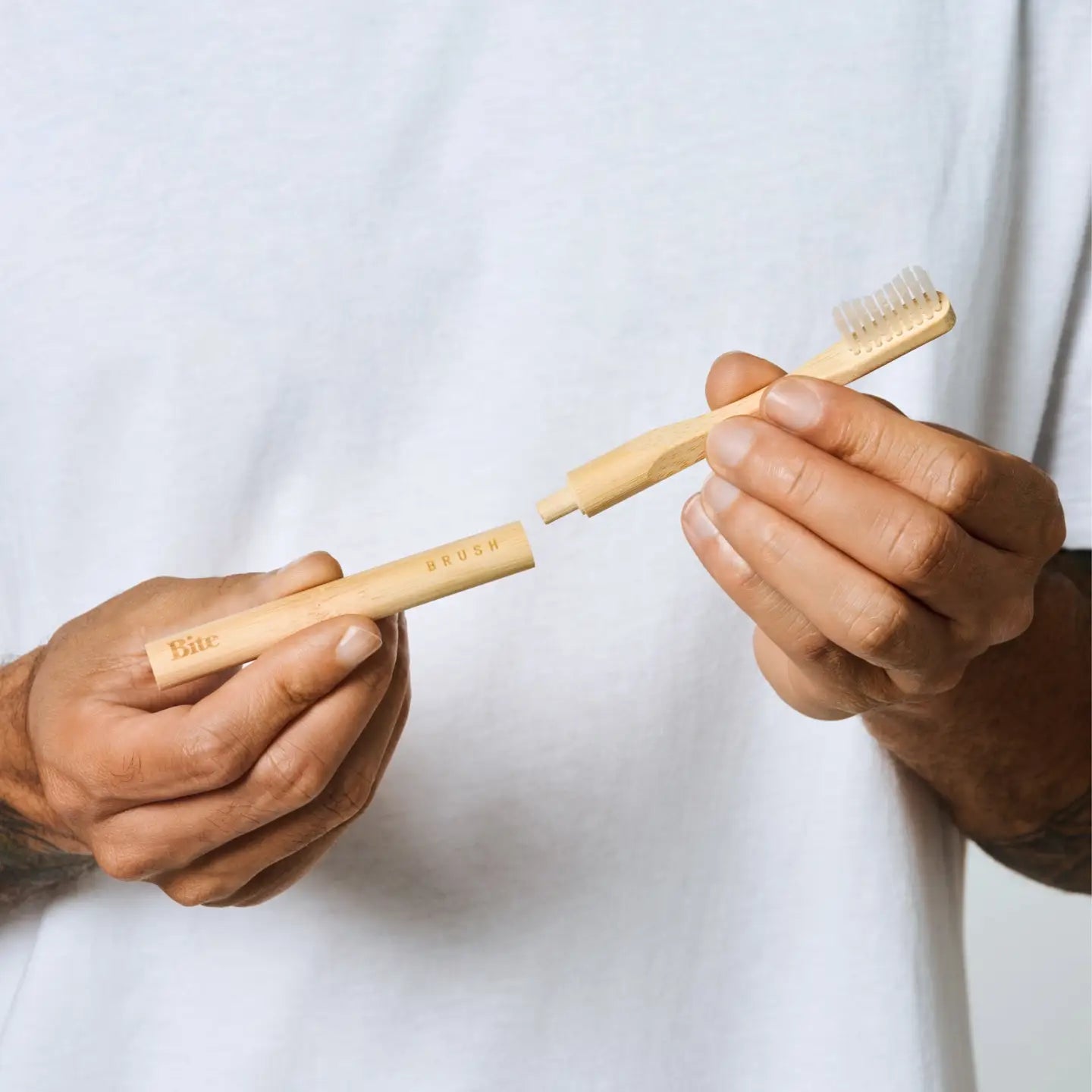 Two hands holding a bamboo toothbrush against a white background