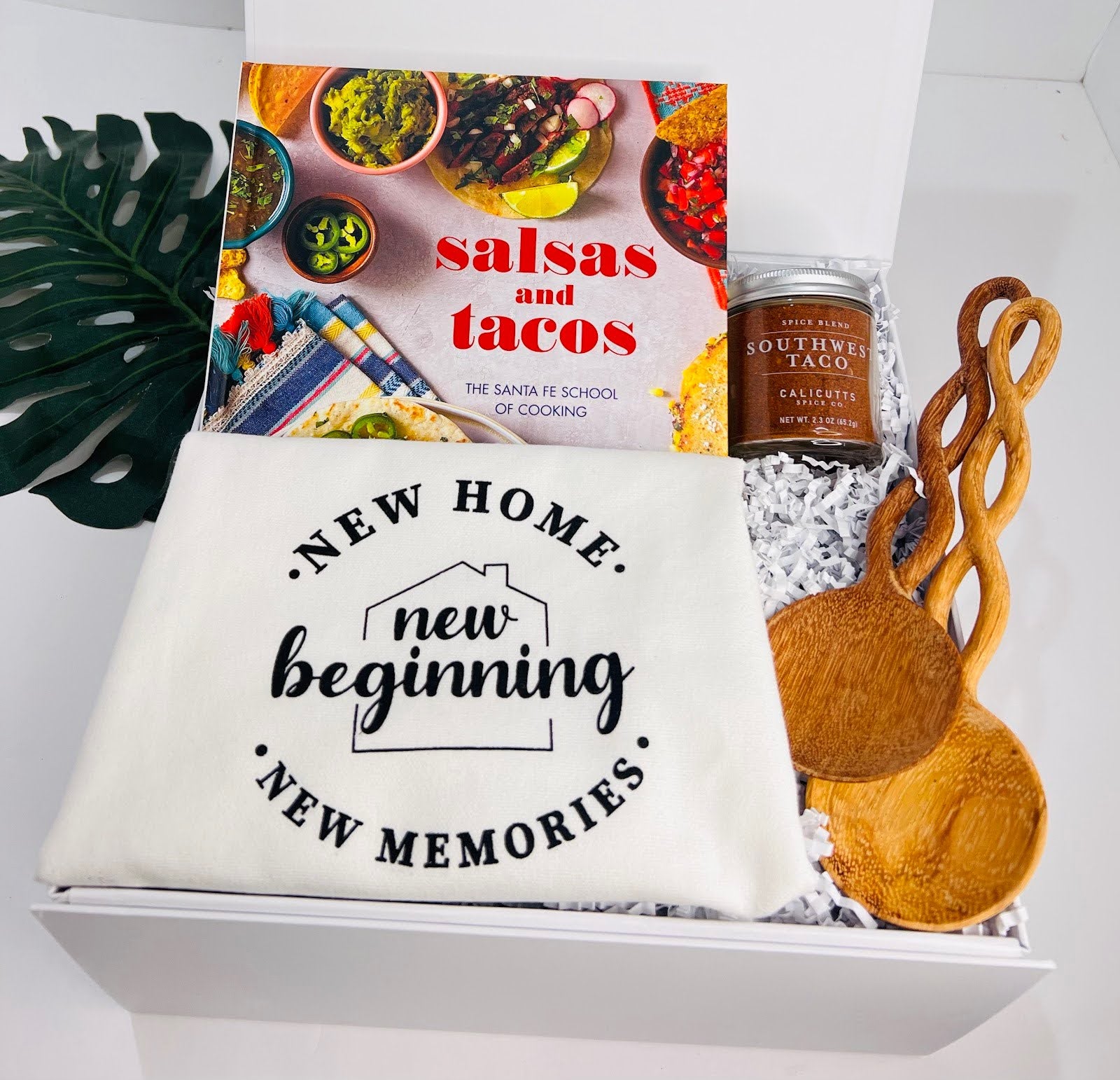 The “Taco ‘Bout a New Beginning” housewarming box by Sonia's Vokalized Kreations includes a "Salsas & Tacos" cookbook, Southwestern Taco Spice Blend, two wooden utensils, and a themed “New Home” kitchen towel.