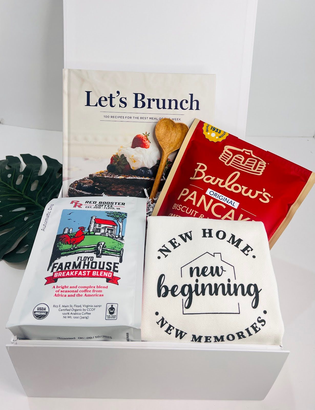 The Let's Brunch Kitchen Housewarming Gift Box by Sonia's Vokalized Kreations includes a “Let’s Brunch” cookbook, wooden spoon, Barlow’s pancake mix, breakfast blend coffee, and a “New Home” towel—ideal for cozy mornings and new beginnings.