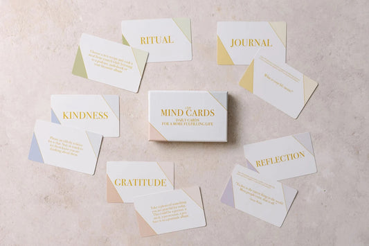 A set of nine "Mind Cards: Daily Cards" by sonia's-vokalized-kreations is arranged on a beige surface, featuring categories like Ritual, Journal, Kindness, Gratitude, and Reflection. Each card includes prompts to foster positive habits and support mental health.